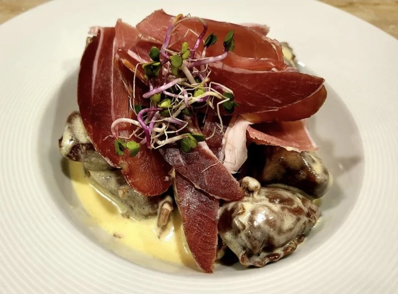 Assiette en sauce crémeuse, garnie de fines tranches de viande séchée et de jeunes pousses.