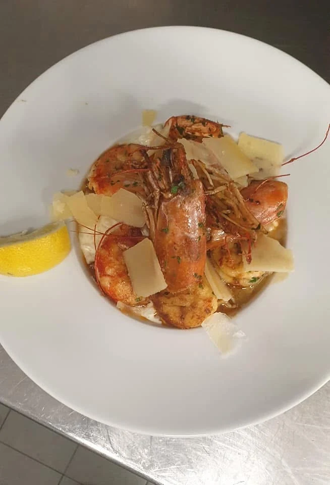 Assiette de gambas avec copeaux de fromage et un quartier de citron.