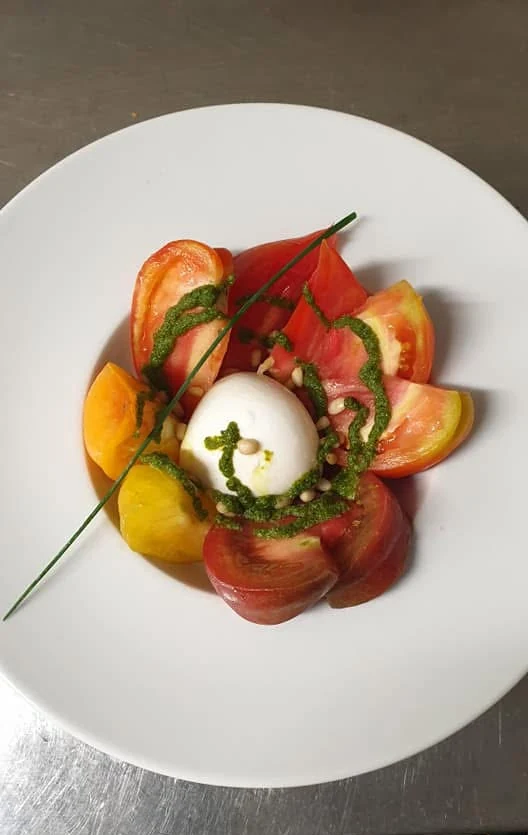 Tomates de différentes couleurs autour d’un fromage frais, avec sauce verte et ciboulette.